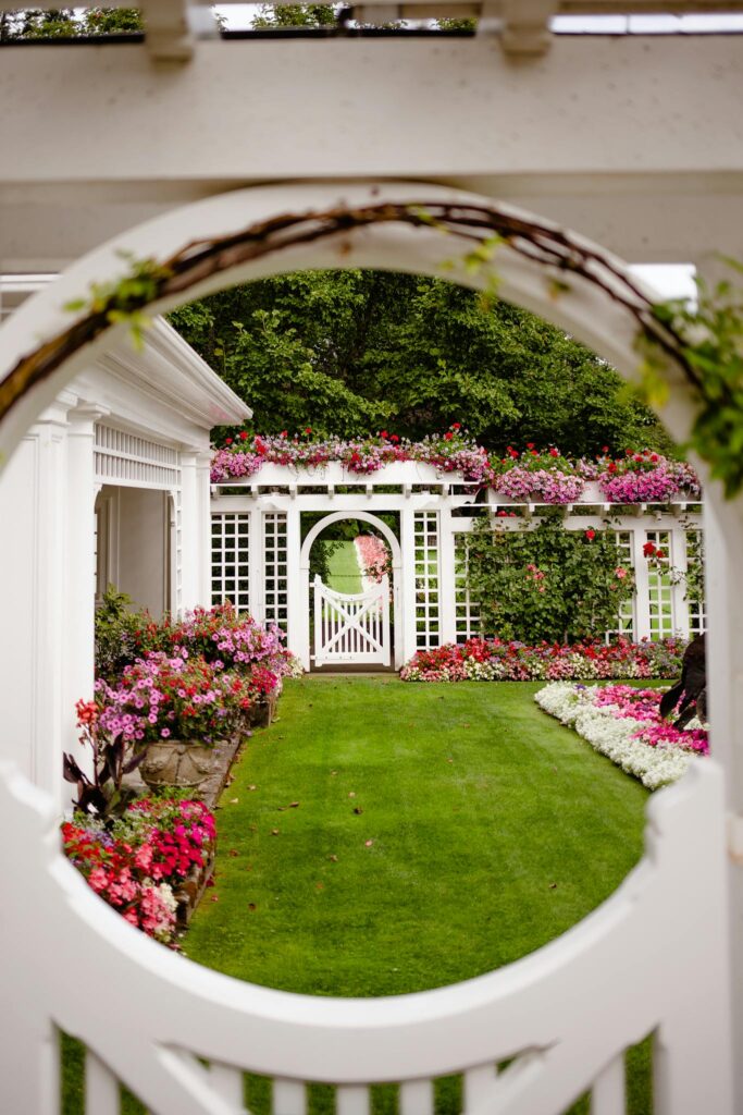 A vibrant garden view framed by a circular gate, featuring blooming flowers and lush greenery.