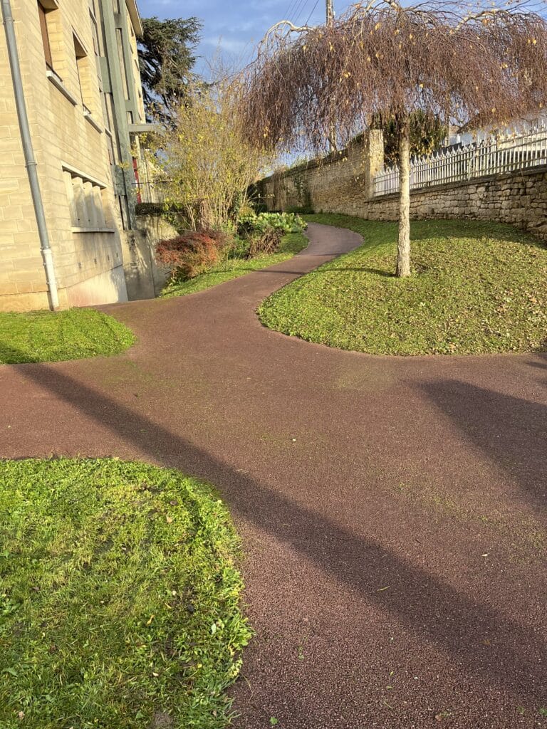 Allée de jardin en gravier rouge bordée de pelouse tondue